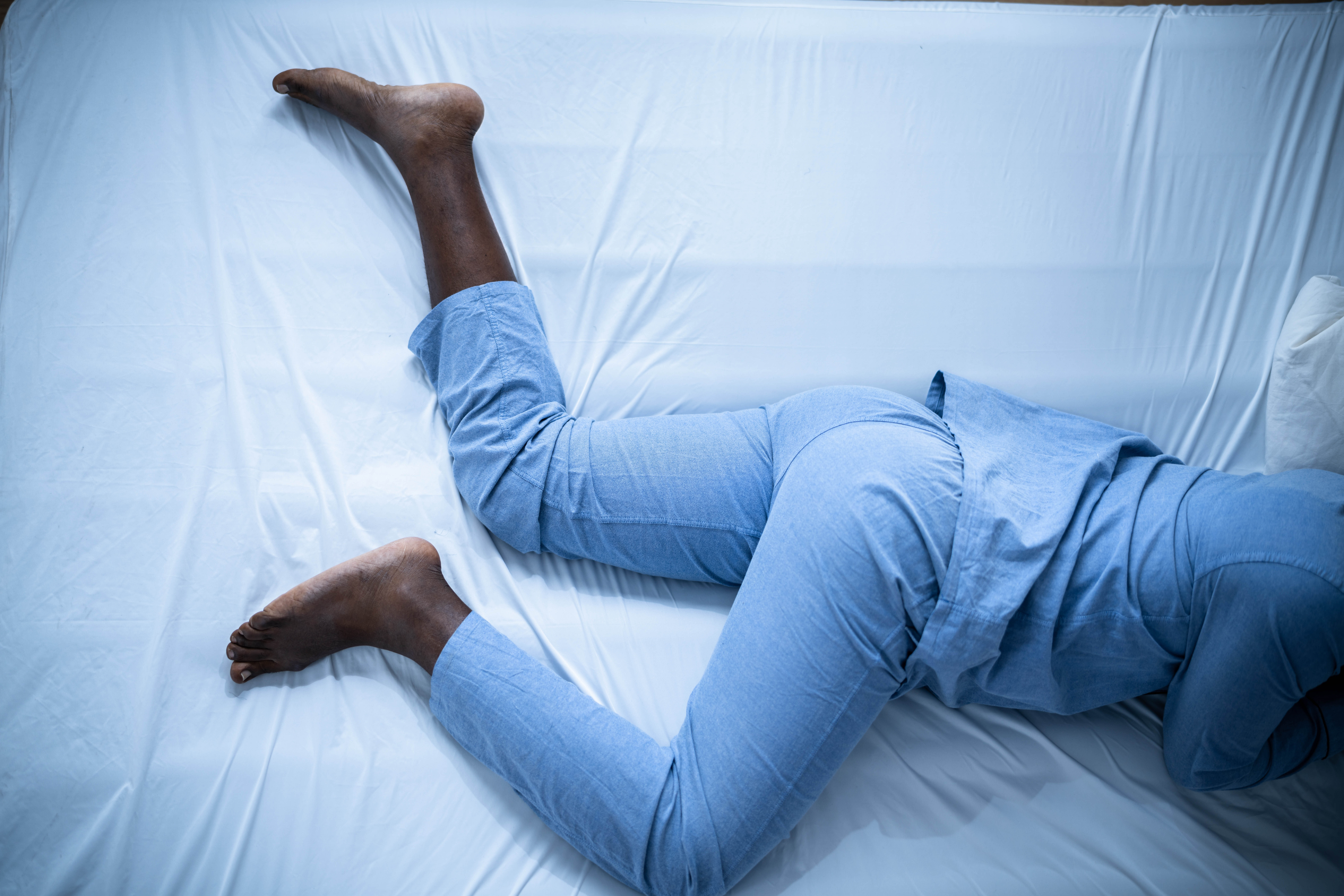 Overhead view of man's legs in bed in movement - highlighting restless leg syndrome Overhead view of man's legs in bed in movement - highlighting restless leg syndrome